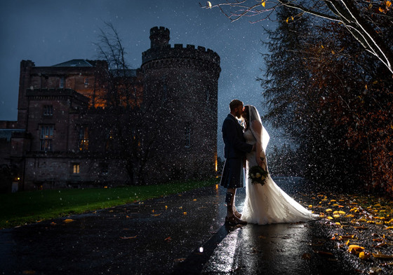 Bride and groom evening kiss in the rain with the shadow of Dalhousie Castle in background